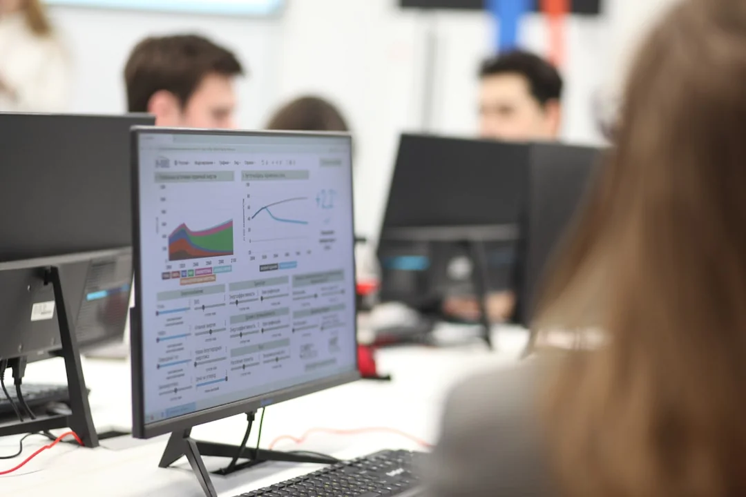Two businessmen review stock market data on a smartphone and laptop in a contemporary office environment.